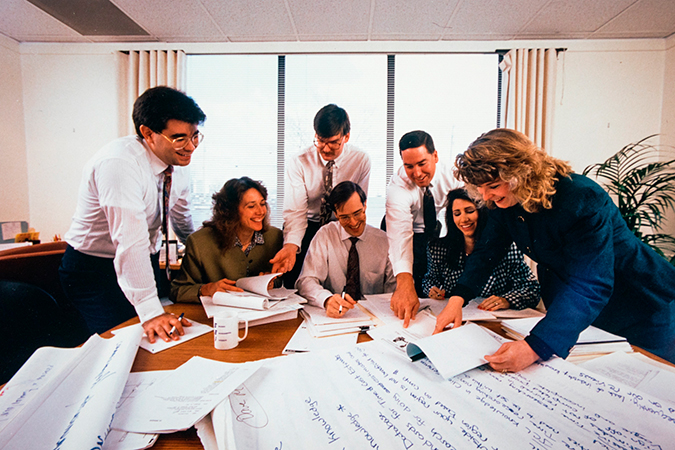 Archival image of colleagues huddled around a conference table.