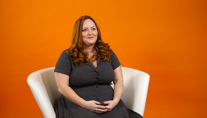 Woman seated in white chair, with orange background color.